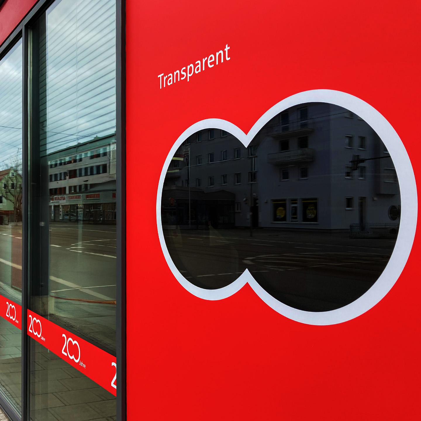 Das 200-Jahre-Logo der Stadtspaarkasse Augsburg als Ausschnitt auf einem Fenster foliert. Daneben steht "Transparent". BRANDSTAGE Design