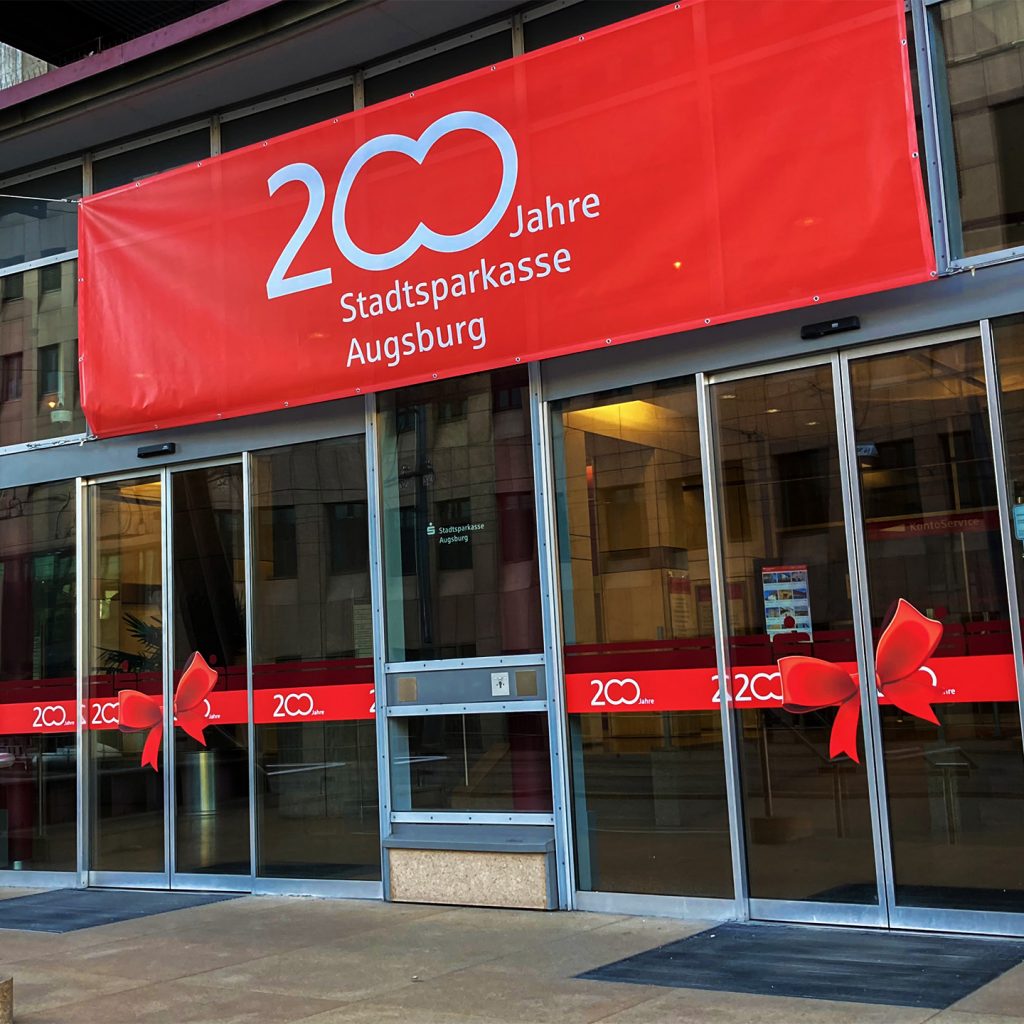 Das 200-Jahre-Logo der Stadtspaarkasse Augsburg auf einem roten Banner über dem Haupteingang der Stadtspaarkasse Augsburg