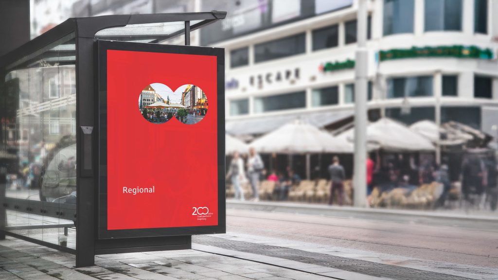 Auf einem Plakat zeigt ein Fernglas ein Bild von Augsburg. Darunter steht "Regional" geschrieben. Danneben zeigt sich das 200-Jahre-Logo der Stadtspaarkasse Augsburg BRANDSTAGE Design