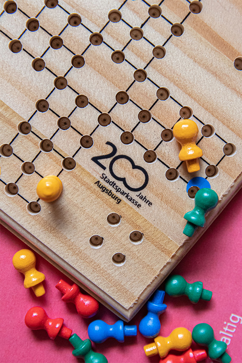 Das 200-Jahre-Logo der Stadtspaarkasse Augsburg auf einem Spielfeld. Bunte Steine liegen neben dem hölzernen Mensch Ärgere Dich Nicht.